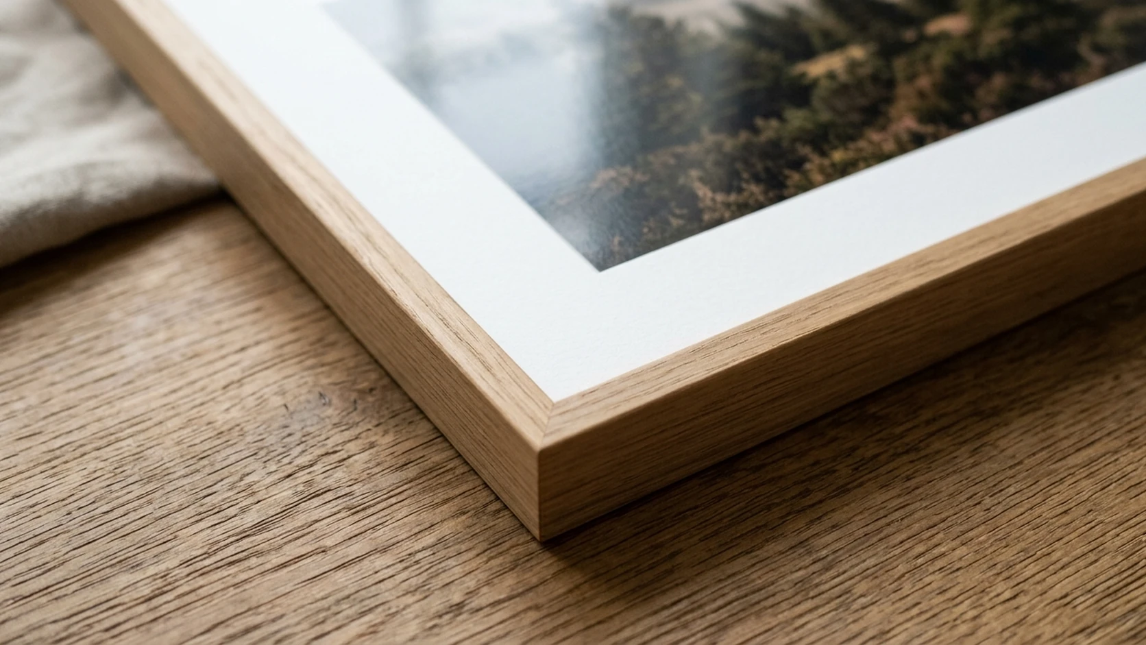 Close-up of an oak frame corner showing the white bevel-cut mat and the edge of the print inside