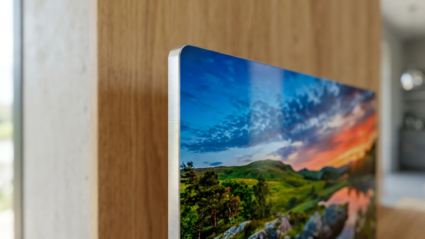 Close-up of the brushed silver edge of a metal print showing the thin aluminum panel, with a sunset landscape photo printed on its face