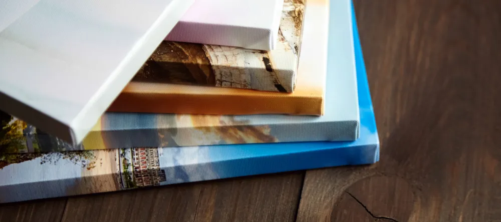 What is canvas made of. Pile of photo canvas prints on table. 
