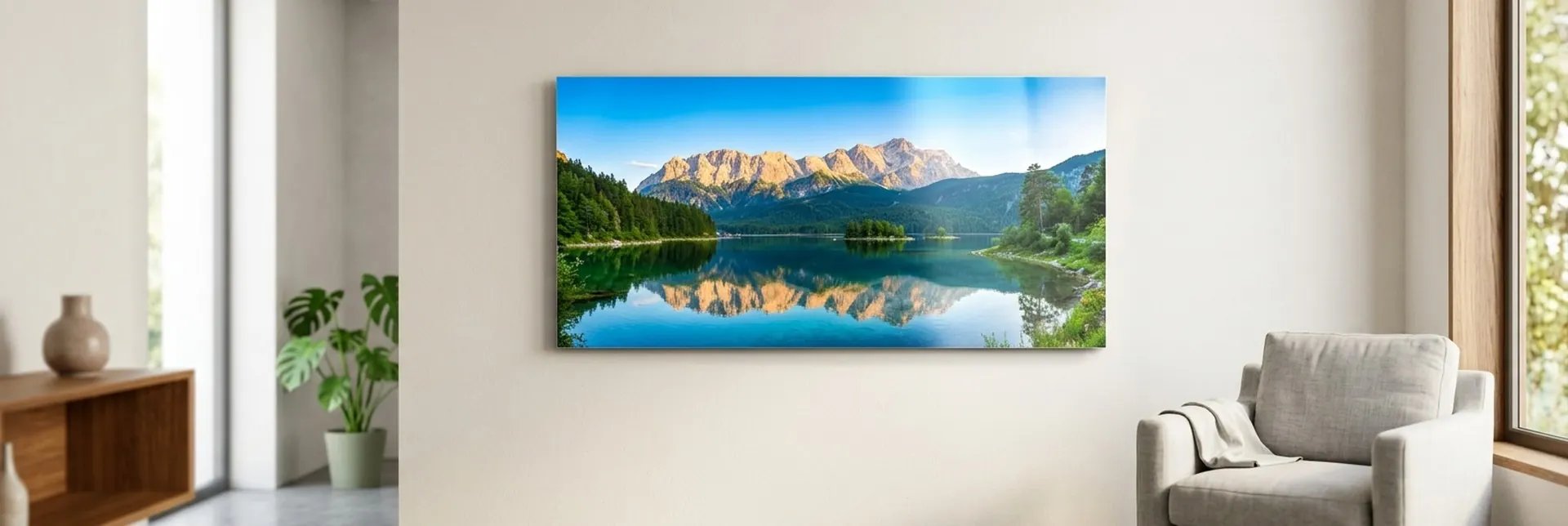 A panoramic metal print of a mountain lake with mirror-still reflections hanging in a bright living room above a wooden sideboard