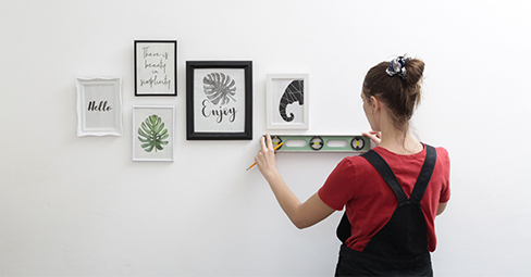 How to Hang Pictures Without Nails. Young Woman Hanging Wall Art.