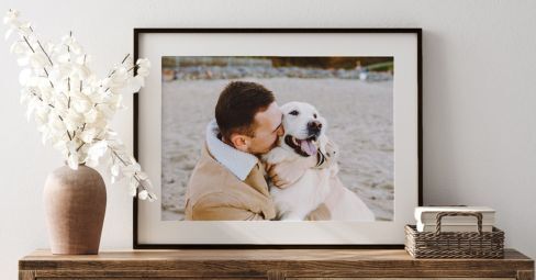Framed beach photo of a man kissing his golden dog, displayed on a wooden sideboard